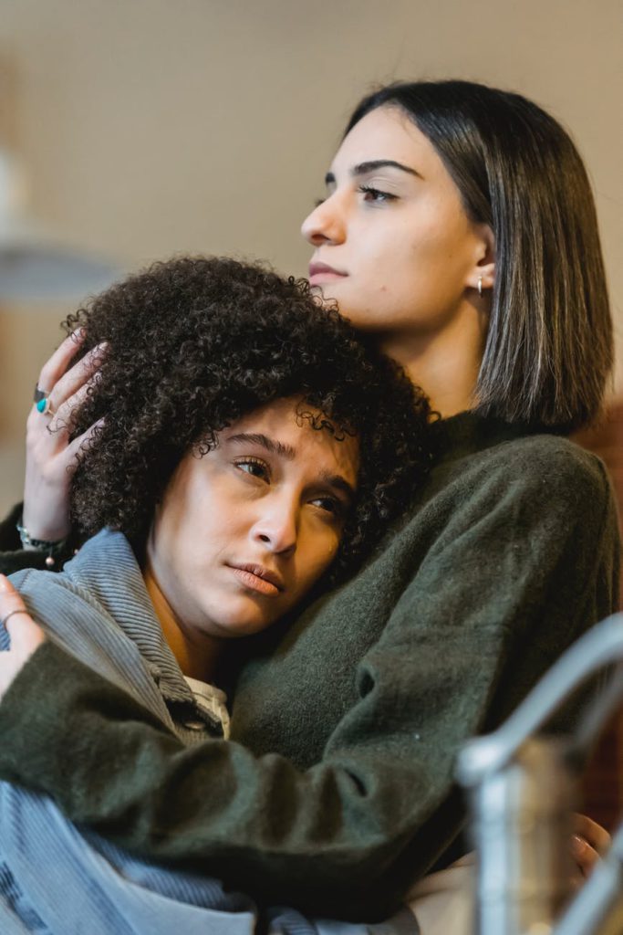 serious young woman embracing sad black girlfriend