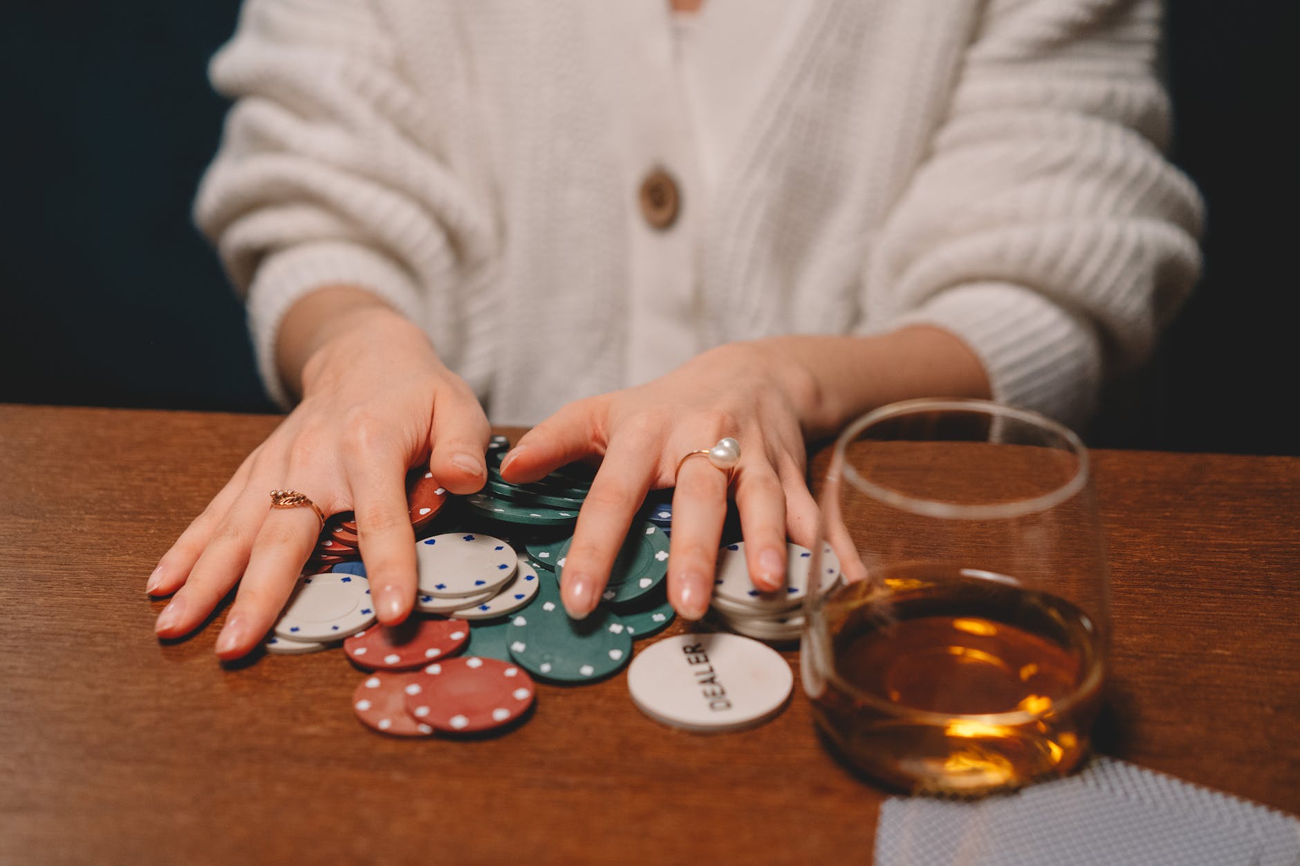 person in white sweater holding poker chips on a wooden table